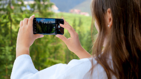 Young woman making photographs of beautiful mountains and pine forest. Concept of people traveling,...