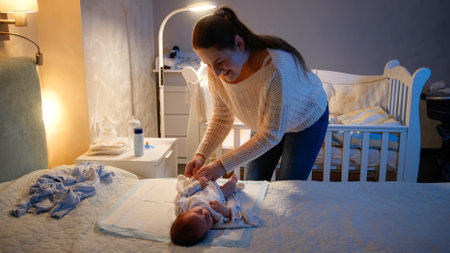 Young caring mother dressing her little baby at night. Parent putting on clothes on newborn child. Concept of loving and caring parents, newborn babies and family happiness.の写真素材
