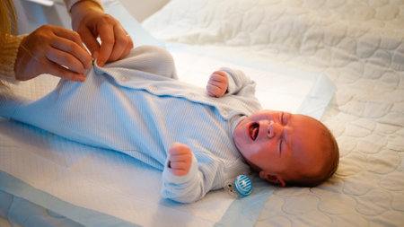 Little newborn baby getting dressed and sucking pacifier on bed at night. caring mother changing...