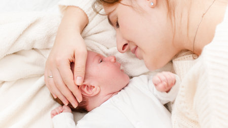Closeup shot of little newborn baby lying next to mother and crying. Happy smiling woman looking at...