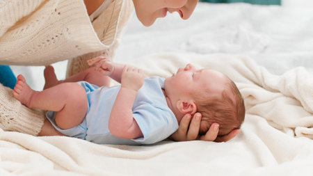 Young caring mother putting her little baby son on soft blanket in bedroom. Concept of family happiness and loving parents with little children.の写真素材