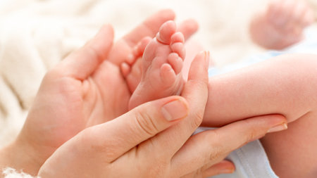 Closeup of woman gently stroking with hand tiny feet of her newborn baby son with perfect skin. Concept of family happiness and loving parents with little childrenの写真素材