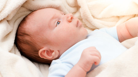 Above view on adorable newborn baby covered in soft blanket lying in crib.