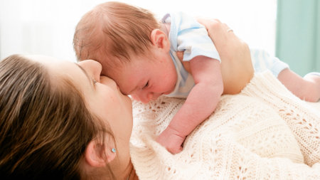 Portrait of little newborn baby boy lying on yougn mother relaxing on bed at home. Caring parents...