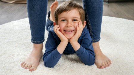 Portrait of happy smiling little boy lying on carpet between mothers feet
