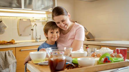 Happy laughing mother with little son hugging on kitchen after cooking dish. Children cooking with parents, little chef, family having time together, domestic kitchen.の写真素材