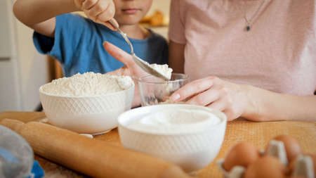 Closeup of little son helping mother pouring flour in bowl for making biscuit or dough. Children...