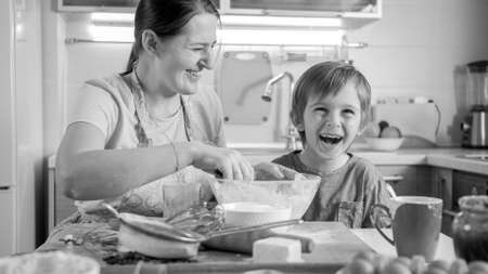 Black and white portrait of laughing boy with mother cooking on kitchenの写真素材