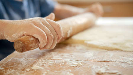 Closeup of little child using wooden rolling pin for preparing pizza dough