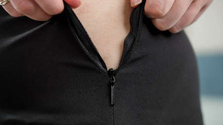 CLoseup of woman pulling stuck zipper on small tight dress. Concept of excessive weight, obese...