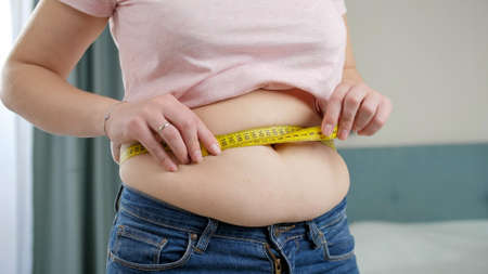 Young obese woman struggling to measure big belly with measuring tape. Concept of excessive weight, obese female, dieting and overweight problemsの写真素材