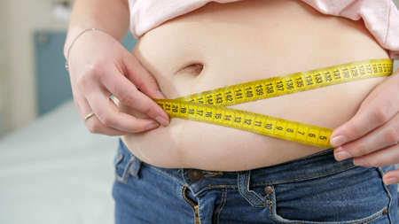 Closeup of young woman loosing weight measuring her waist. Concept of dieting, unhealthy lifestyle,...