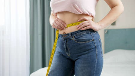 Beautiful slim woman measuring her waistline with yellow measuring tape. Concept of dieting, loosing weight and healthy lifestyle.の写真素材