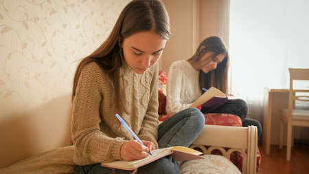 Two teenage sister doing homework and writing in copybooks. Teens studyingの写真素材