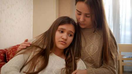 Teenage girl consoling and stroking her upset girl friend talking about problems in relationships. Friends support and teenager depressionの写真素材