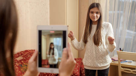 SMiling teenage girl dancing in front of smartphone recording video for posting in internet. Modern communication, social media and gadgetsの写真素材