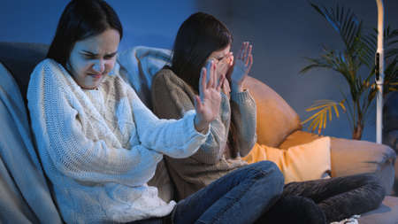 Young girls closing eyes and feeling disgusted while watching horror or scary show on TV