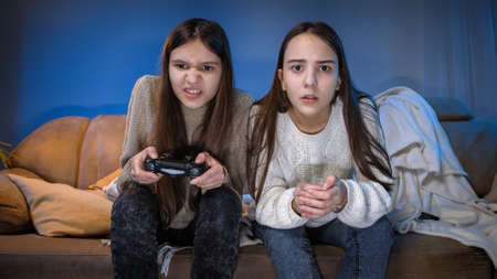 Two concentrated girls playing video games on game console in living room at nightの写真素材