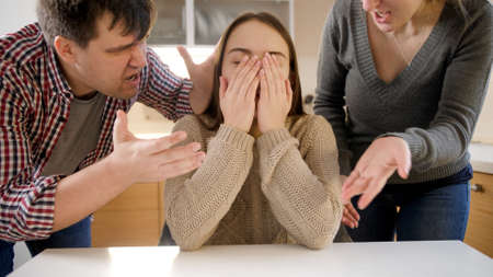 Teenage girl crying and closing face with hands after conflict with parents. Family violence, conflicts and relationship problemsの写真素材
