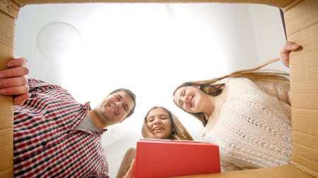 Happy teenage girl opening big cardboard box, taking out gift or present and kissing parents