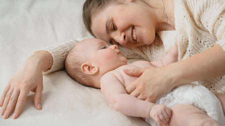 Cute little baby boy touching his smiling mother lying next to him in bed. Concept of parenting ,baby care and family happinessの写真素材