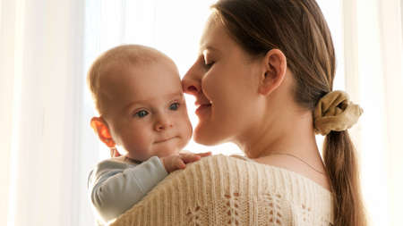 Portrait of little baby and smiling mother hugging at home. Concept of family happiness and...