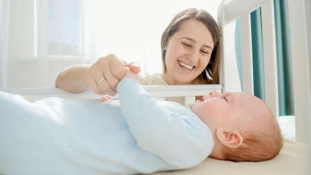 Smiling caring and loving mother stroking her little baby in cradle. Concept of parenting, family...