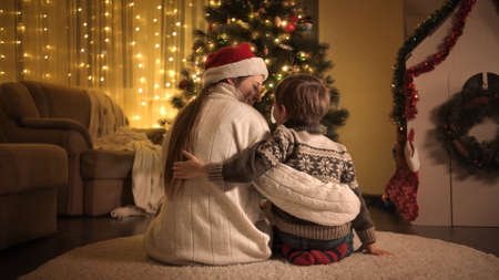 Little boy with mother sitting on floor in living room and looking on Christmas tree. Families and children celebrating winter holidays.の写真素材