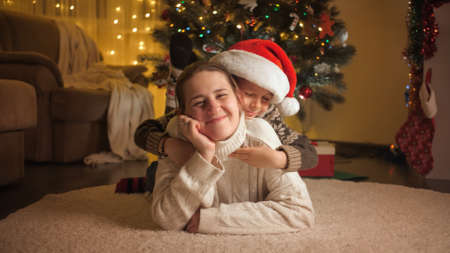 Cute boy with mother relaxing on floor and hugging next to Christmas tree. Pure emotions of families and children celebrating winter holidays.の写真素材