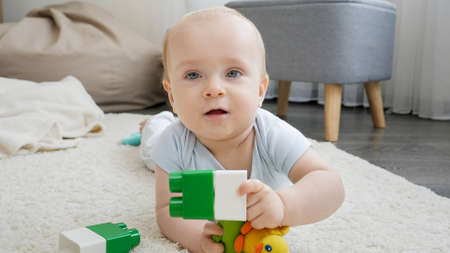 Little smiling baby boy palying and having fun with toy blocks and toy on floor at living room. Concept of children development, education and creativity at homeの写真素材