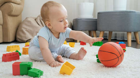 Happy smiling baby boy playing with toys and basketball on carpet at home. Concept of children development, sports, education and creativity at homeの写真素材
