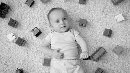 Black adn white portrait of cute baby boy palying with colroful bricks and blocks looking up in camera. Concept of children development, education and creativity at homeの写真素材
