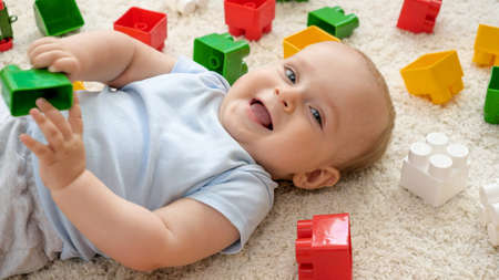 Smiling baby boy and heap of toys on carpet in playroom. Concept of children development, education and creativity at homeの写真素材