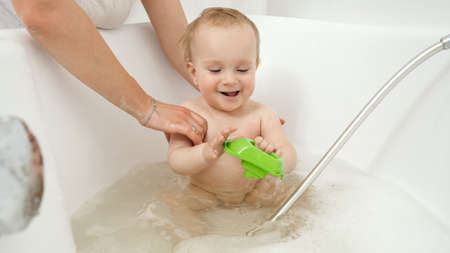 Happy smiling baby boy enjoying washing in bath and playing with toys. Concept of children hygiene,...