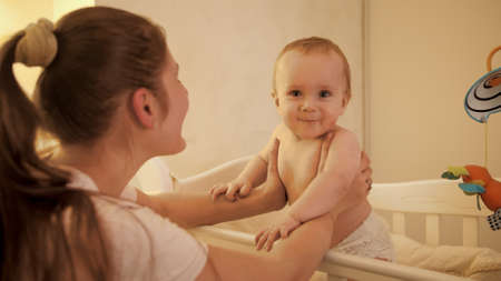 Portrait of adorbale smiling baby boy in diapers standing in bed at night