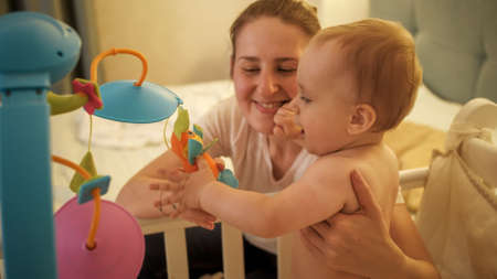 Cute smiling baby boy with mother playing toys in bed before going to sleep.