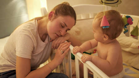 Portrait of tired mother leaning on bed side and sleeping next to her baby sonの写真素材