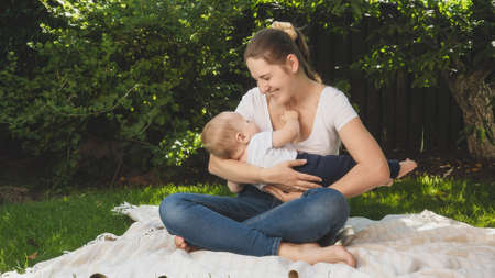 Happy smiling mother holding her baby son and smiling at him in backyard garden. Parenting, family, children development, and fun outdoors on nature.の写真素材