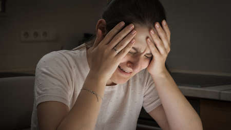 Portrait of despaired crying woman sitting on kitchen at night. Concept of despair, stress, depression, anxiety and frustration.の写真素材