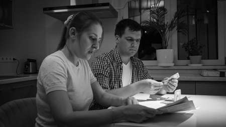Black adn white portrait of worried and stressed couple counting money on kitchen at nightの写真素材