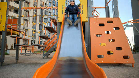 Happy cheerful boy riding on slide on playground and smiling in camera. Concept of child development, sports and education.の写真素材