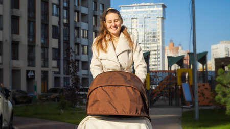 Portrait of smiling mother walking with her baby in stroller on sunny windy dayの写真素材