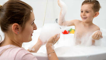Cheerful boy with mother having fight with soap foam in bath. Concept of hygine, children...