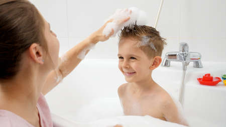 Happy smiling mother with son playing in bathroom and making stylish haircuts with soap foam. Concept of hygine, children development and fun at homeの写真素材
