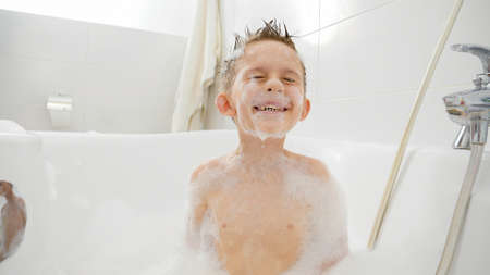 Funny shot of little boy diving under water in bath full of soap foam and sudsの写真素材