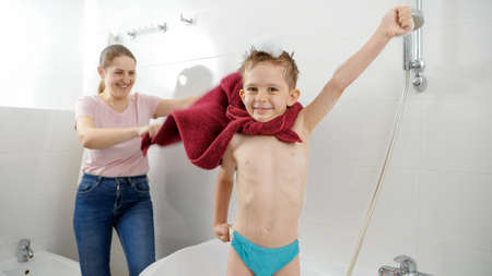 Funny little boy pretending to be superhero with mother in bathroom. Concept of family time, children development and fun at homeの写真素材