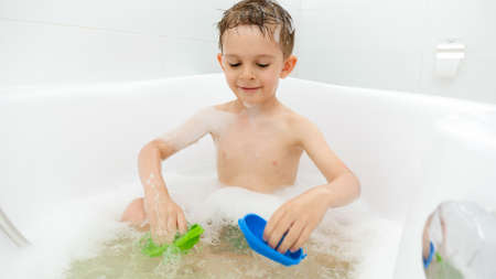 Cute boy enjoying bathing with soap foam and playing toys. Concept of family time, children development and fun at homeの写真素材