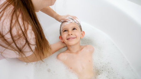 Little smiling boy with mother washing head in bathの写真素材