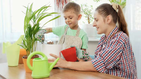 Smiling little boy with young mother planting flowers in pots at homeの写真素材