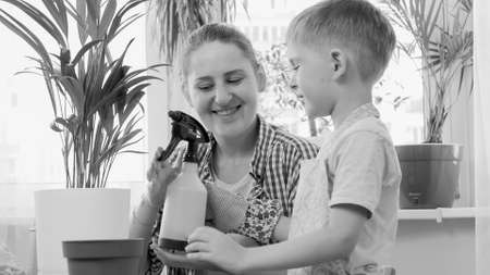 Black and white portrait of mother giving sprinkler to her little son for watering domestic flowers...